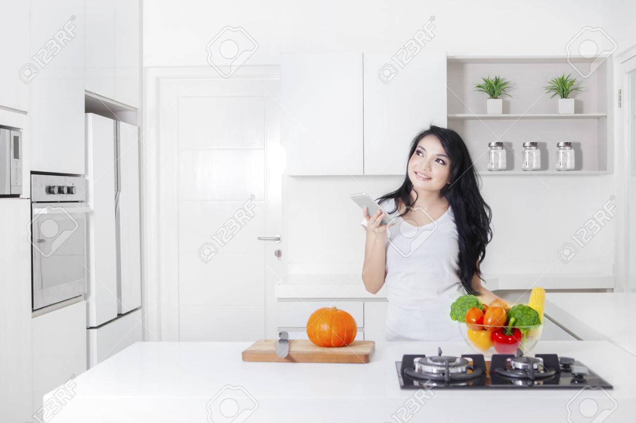 young woman cooking in the kitchen while holding a mobile phone