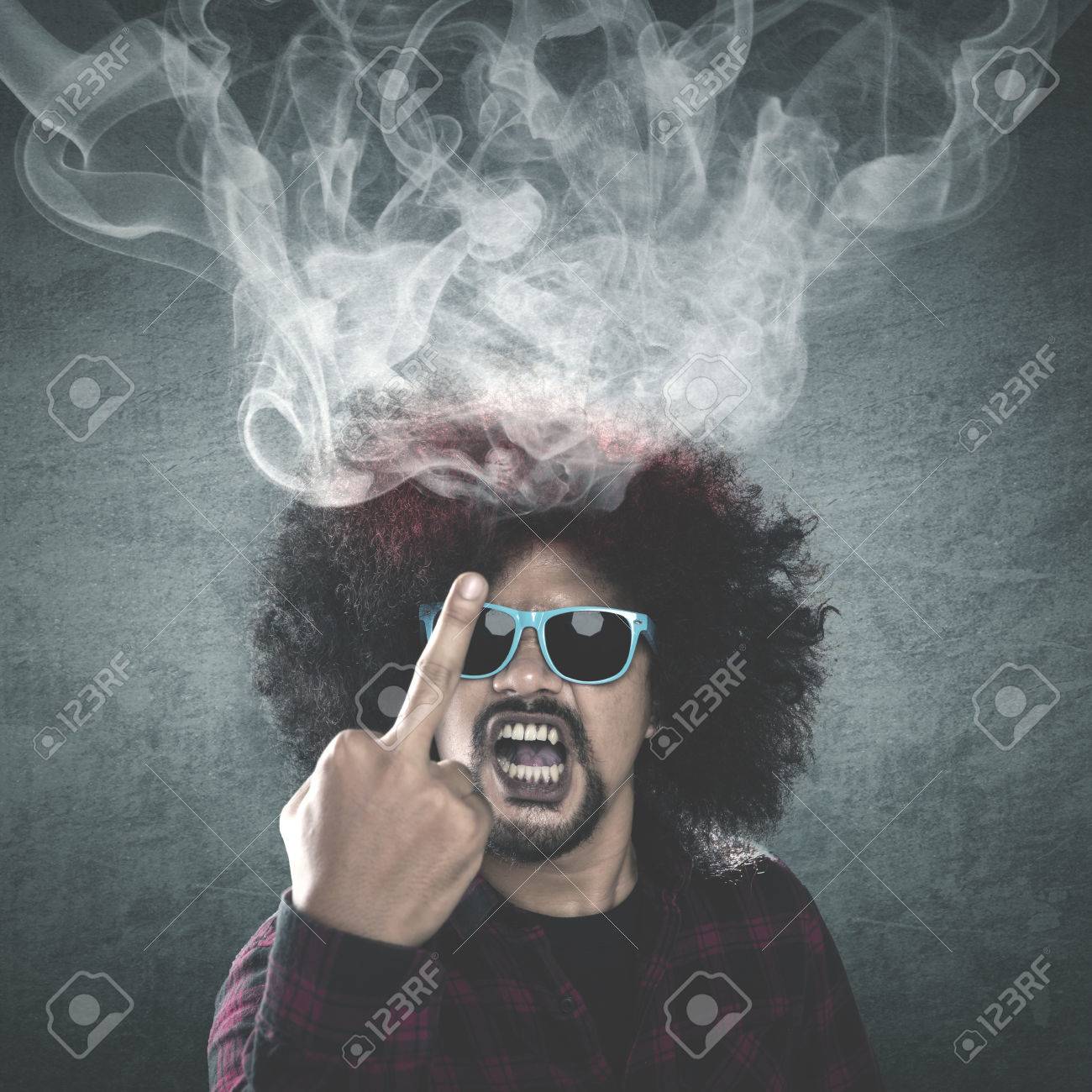 巻き毛を持つ黒人の男に見えます怒ってと失礼な頭から出てくる煙に中指を表示 の写真素材 画像素材 Image
