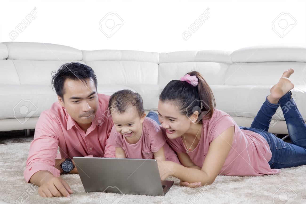 カーペットの上で一緒に横たわってノートパソコンで遊ぶ幸せな家族の画像 の写真素材 画像素材 Image