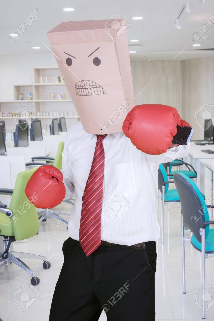 頭に紙袋をかぶり ボクシンググローブを着用し カメラに向かって攻撃する男性起業家 オフィスで撮影 の写真素材 画像素材 Image