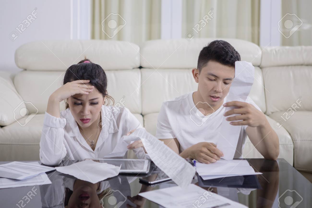 Picture of young sad couple checking their high expenses while sitting at home - 112967727 Picture of young sad couple checking their high expenses while sitting at home - 112967727