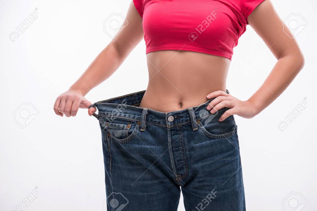 Close-up of slim waist of young woman in big jeans showing successful weight loss, isolated on white background, diet concept - 34868822 Close-up of slim waist of young woman in big jeans showing successful weight loss, isolated on white background, diet concept - 34868822