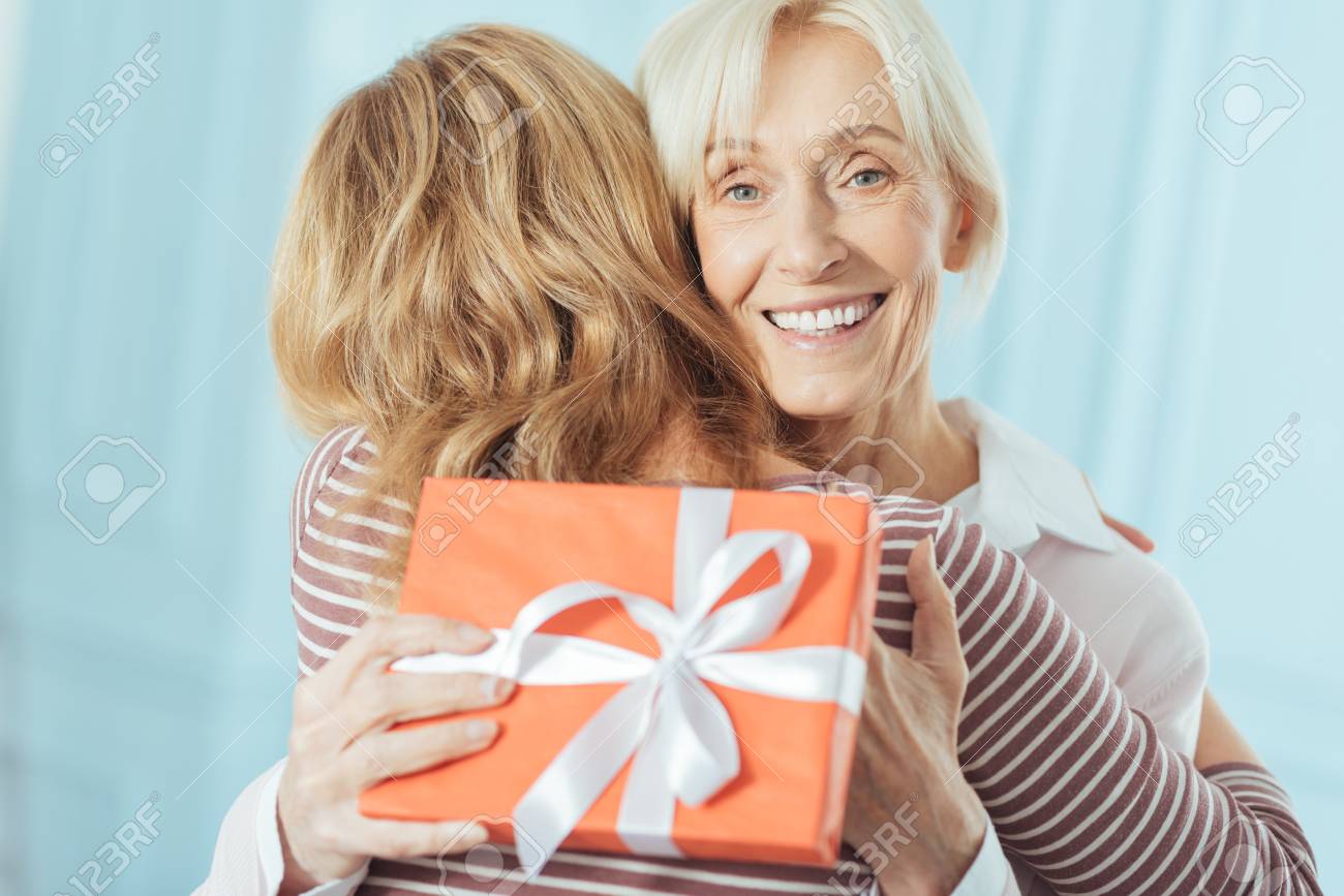 寛大なプレゼント 彼女の気遣う思いやりのある孫娘から素晴らしいプレゼントを得た後 感情的な陽気な先輩女性は興奮し 幸せを感じています の写真素材 画像素材 Image