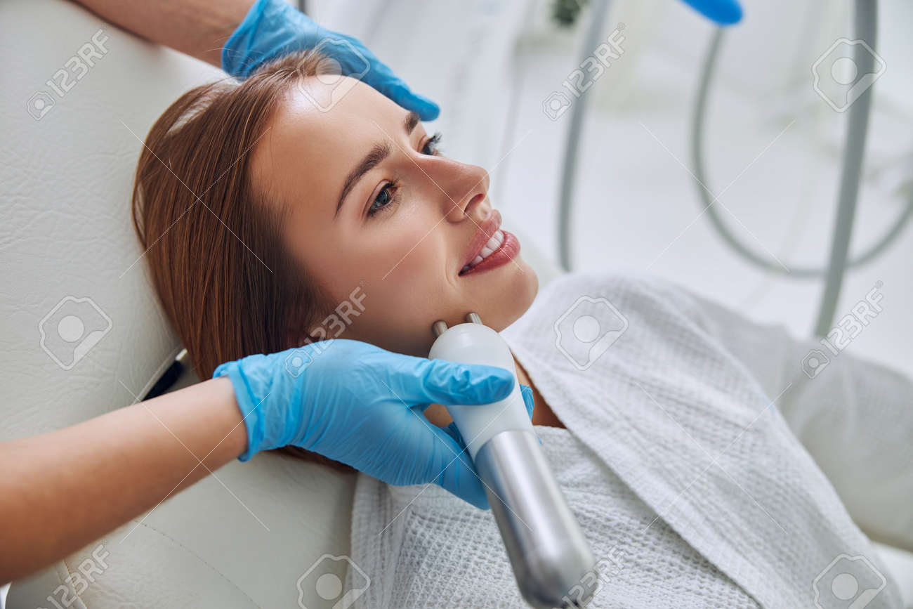 Redheaded female lying on medicine chair during spa skin treatment in wellness center - 168303338 Redheaded female lying on medicine chair during spa skin treatment in wellness center - 168303338