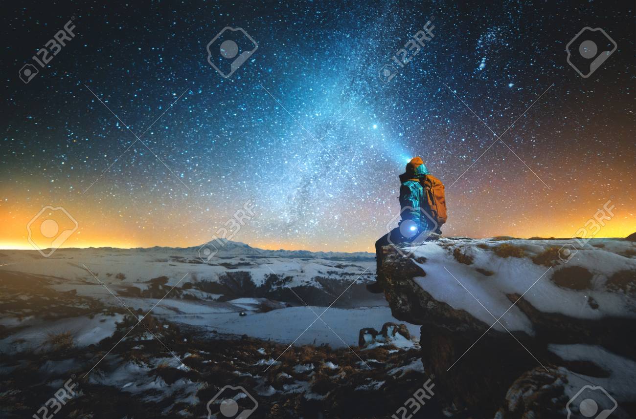Night winter landscape a man with a backpack and a lantern on his head sits on a rock in the mountains in winter against the background of a mountain and a winter starry sky and the Milky Way - 120184877 Night winter landscape a man with a backpack and a lantern on his head sits on a rock in the mountains in winter against the background of a mountain and a winter starry sky and the Milky Way - 120184877