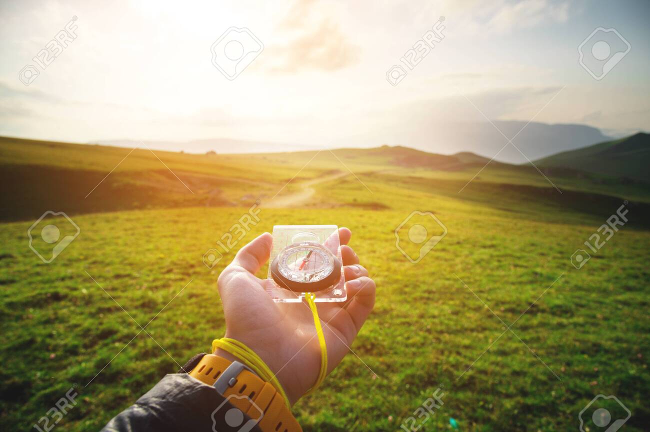 Male hand with a magnetic compass ea against the backdrop of a beautiful landscape at sunset. The concept of navigating the search for your own path and orientation to the cardinal points - 129415459 Male hand with a magnetic compass ea against the backdrop of a beautiful landscape at sunset. The concept of navigating the search for your own path and orientation to the cardinal points - 129415459