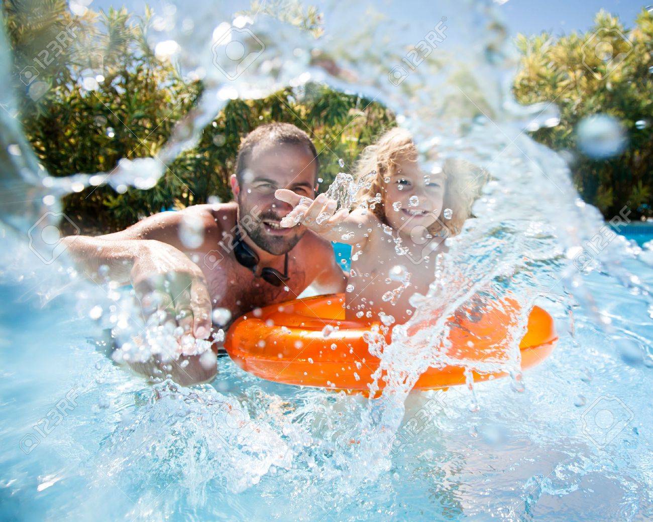 Happy family playing in blue water of swimming pool on a tropical resort at the sea. Focus on children`s hand and splash, shot was taken with waterproof box - 12787464 Happy family playing in blue water of swimming pool on a tropical resort at the sea. Focus on children`s hand and splash, shot was taken with waterproof box - 12787464