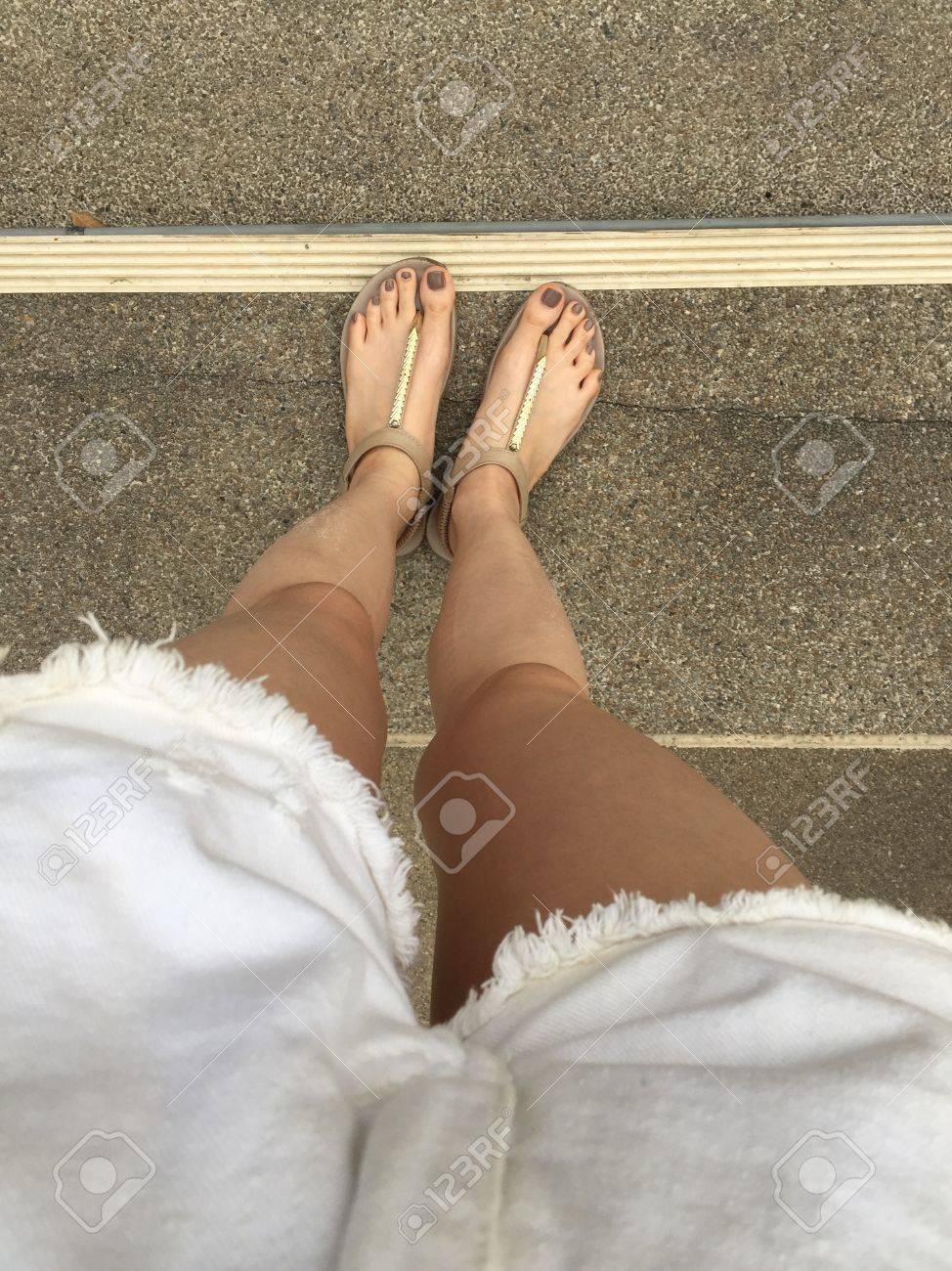 young girl feet with brown nails in gold sandals on staircase