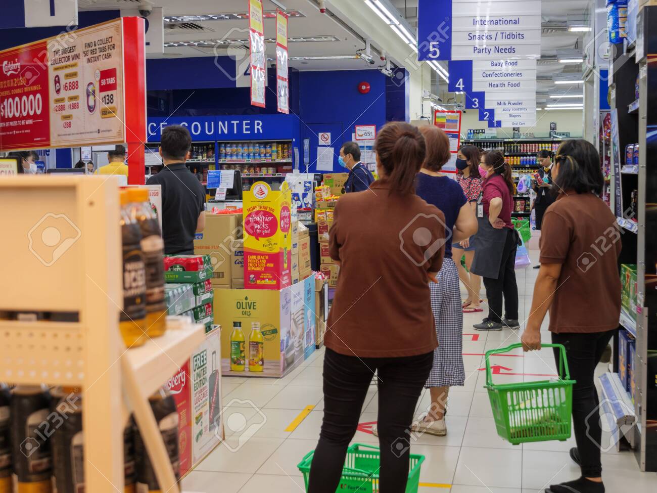 SINGAPORE Â€“ 2 APR 2020 Â€“ Grocery Shoppers Practise Social Distancing As  They Queue To Make Payment At NTUC FairPrice Supermarket. Social Distancing  Markets Are Visible On The Floor Stock Photo, Picture