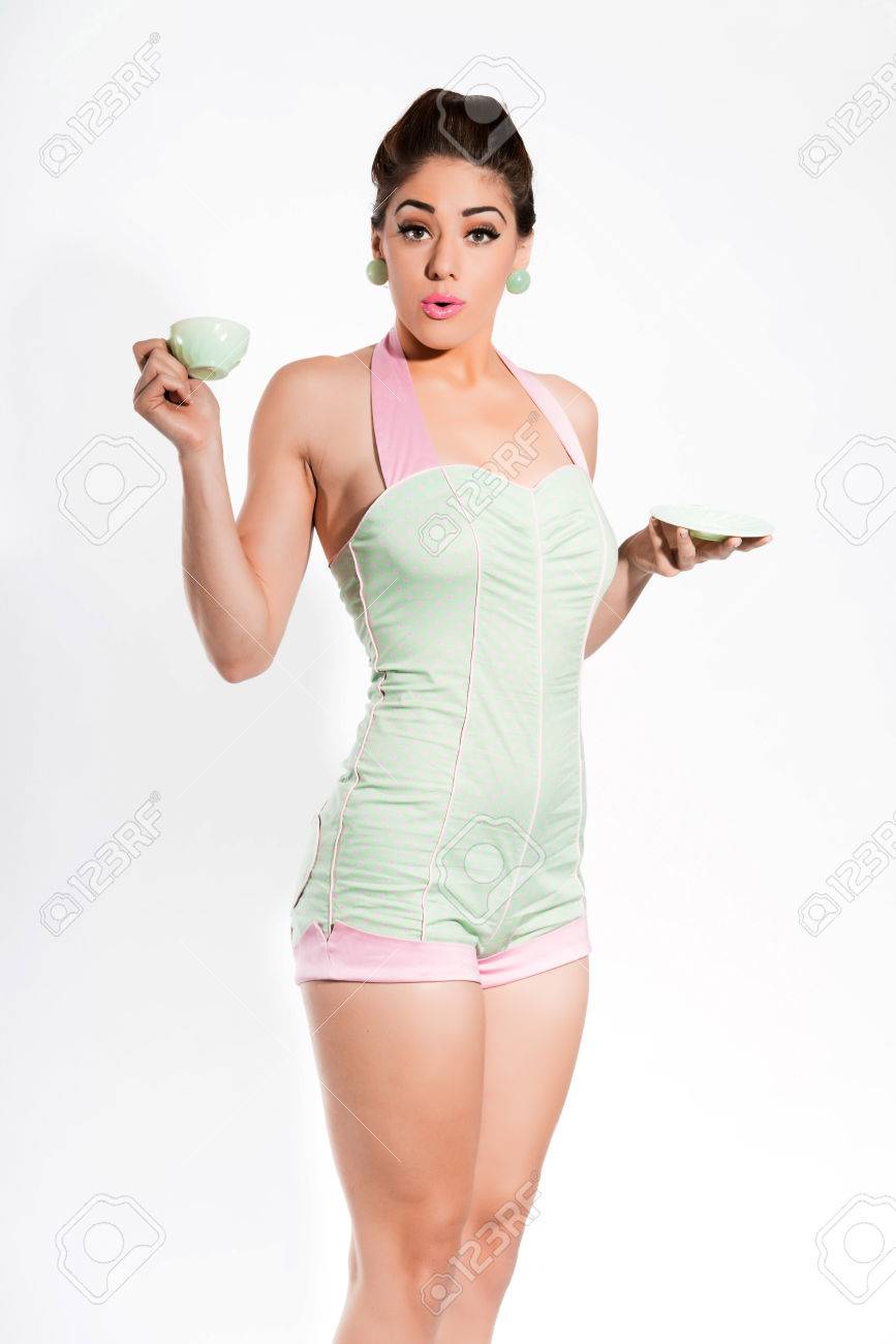 セクシーな 50 代緑とピンクのスーツを身に着けているピンクの口紅とピンナップ ガール 茶の緑のカップを保持しています 前に白い壁 の写真素材 画像素材 Image