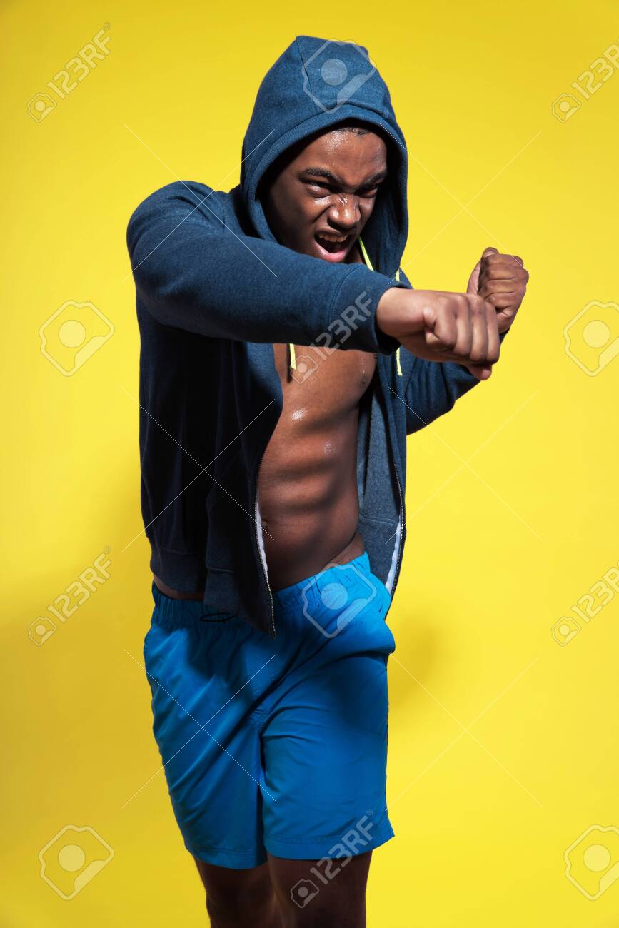 スポーツウェア ファッション青い半ズボンとフーディ運動の黒人男性 ボクシングのポーズ 強烈な色 スタジオ撮影黄色 の写真素材 画像素材 Image