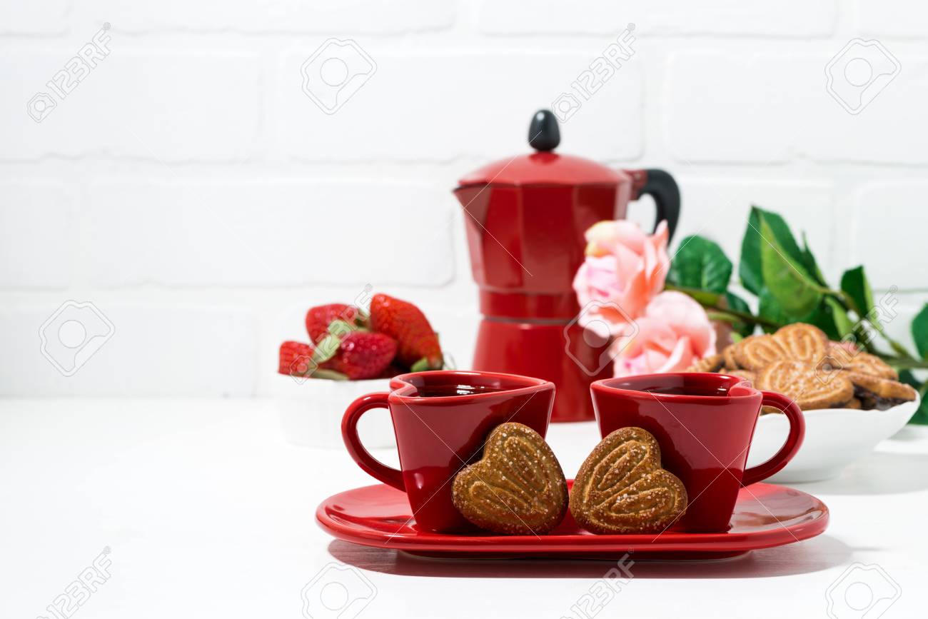 two red coffee cups and heart shaped cookies on white background