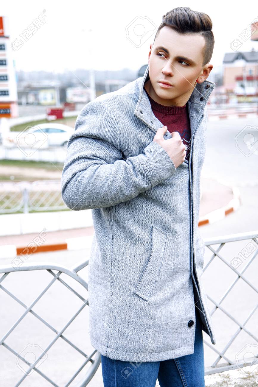 Hombre Joven De Moda Vestido Con Suéter Rojo, Pantalones Vaqueros Y Abrigo Gris De Pie En La Calle. Fotos, Retratos, Y Fotografía De Archivo Libres De Image 77977410.