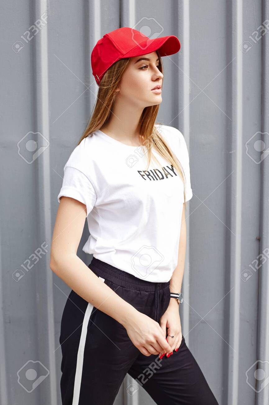 Attractive Blonde Wearing A Red Cap T Shirt And Pants Stands Near A Gray Metal Wall Stock Photo Picture And Royalty Free Image Image 128487961