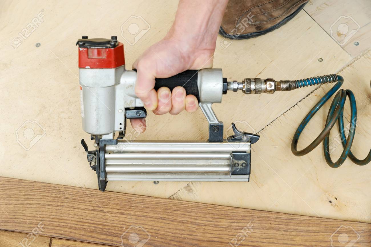 Installing A Wooden Floor A Worker Fixes The Board Using A Nail