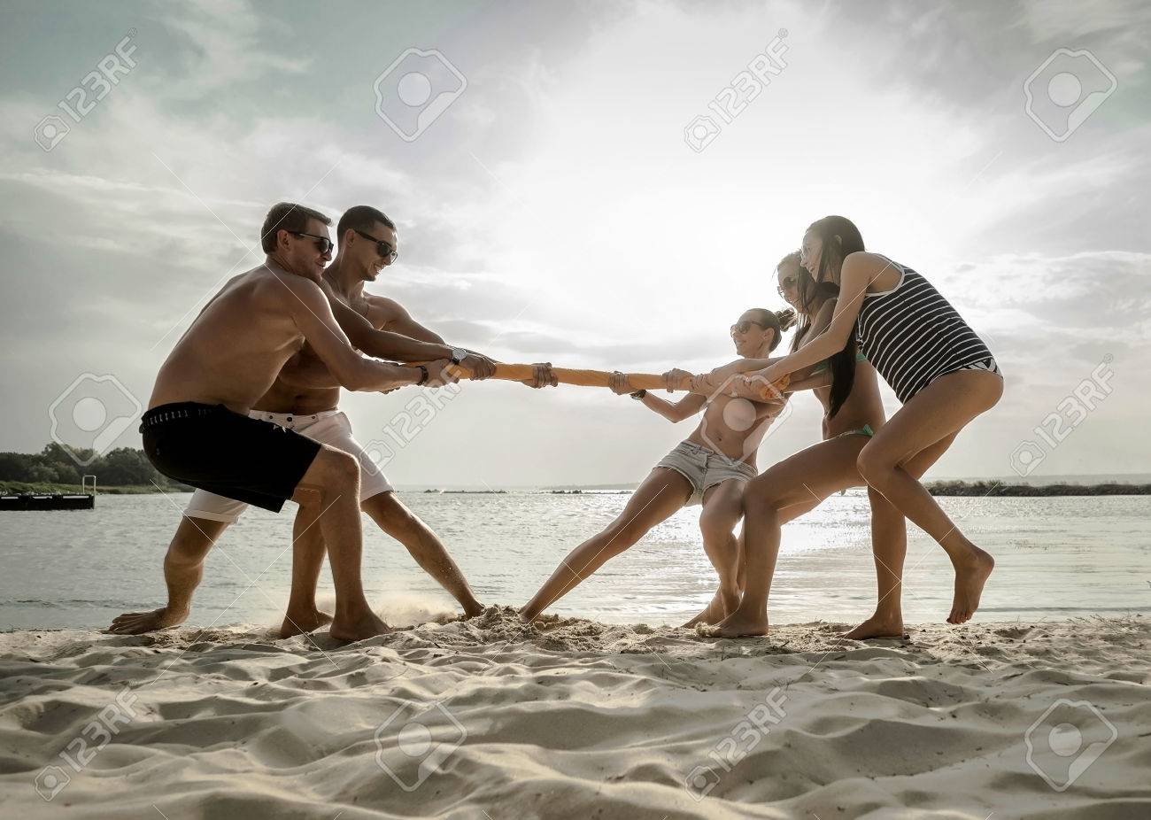 Friends Funny Tug Of War On The Beach Under Sunset Sunlight