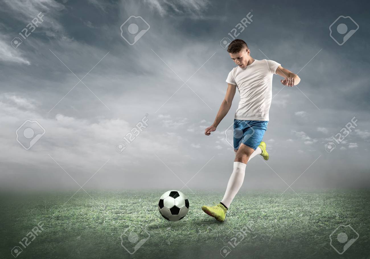 雲と空の下で夏の日にダイナミックなアクションでサッカー場のサッカー選手 スポーティな男は 屋外でボールを撮影しています の写真素材 画像素材 Image