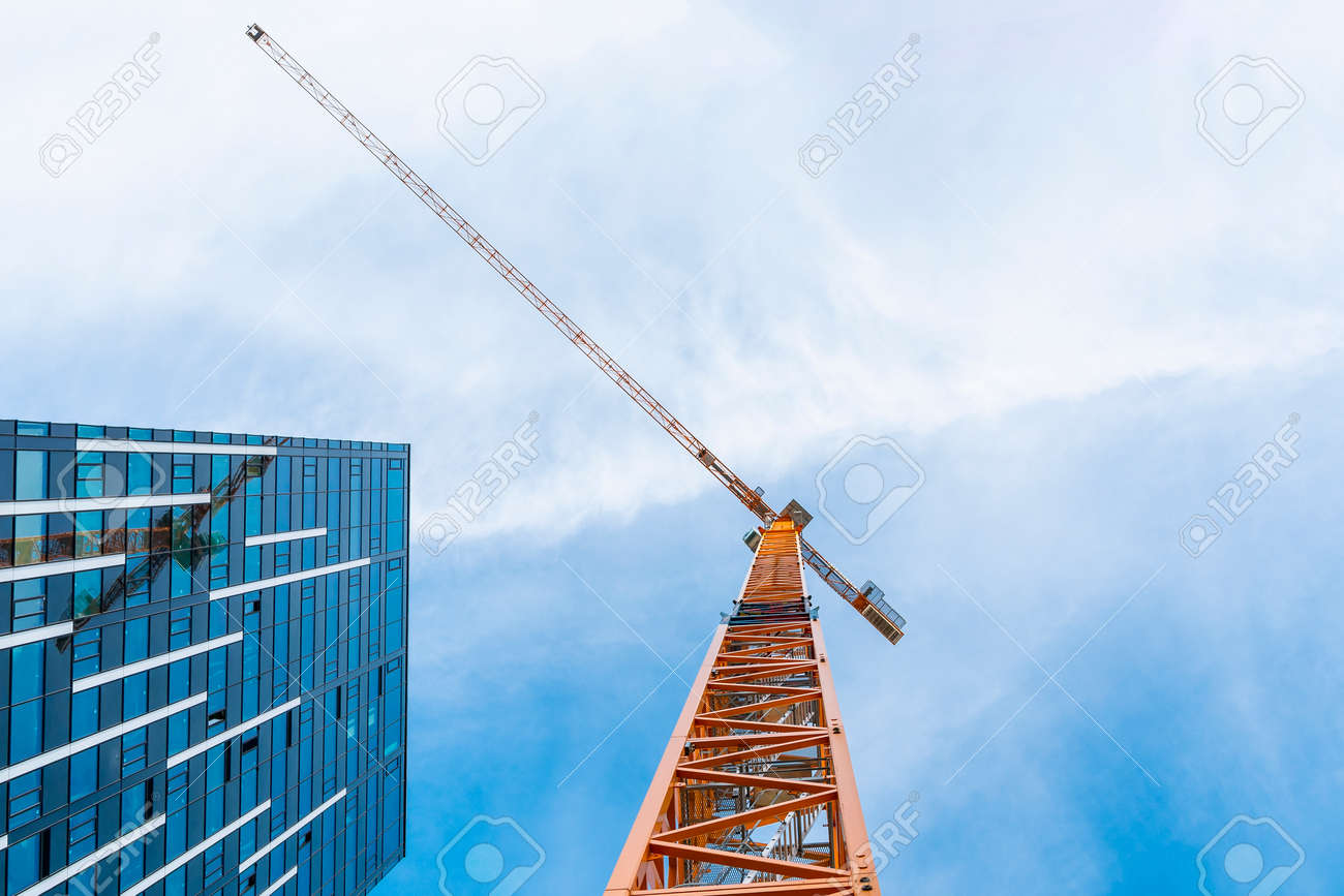 Yellow tower crane. Bottom view of a tall construction crane next to a modern building. - 155600896 Yellow tower crane. Bottom view of a tall construction crane next to a modern building. - 155600896