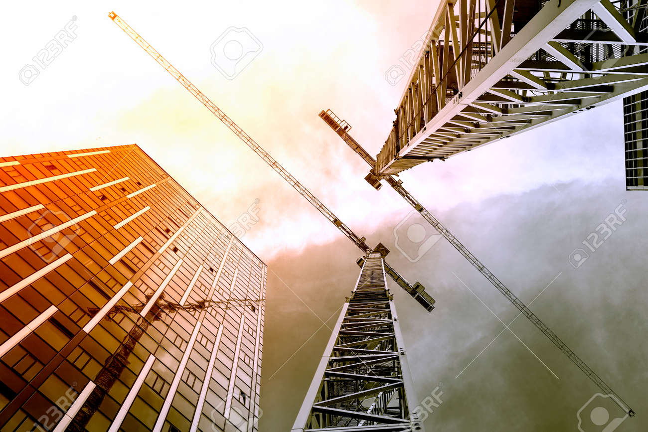 Tower crane. Bottom view of a tall construction cranes next to a modern building. Engineering and architecture design background - 155959144 Tower crane. Bottom view of a tall construction cranes next to a modern building. Engineering and architecture design background - 155959144