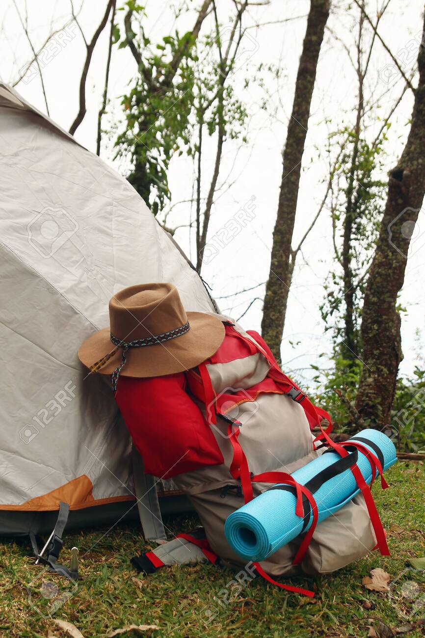 Una Mochila Con Una Y Un Sombrero Cerca De Una Carpa Sobre Un Césped Camping Sobre Un Fondo De Bosque. Fotos, Retratos, Imágenes Y Fotografía Archivo Libres De