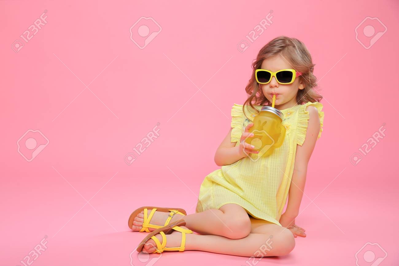 Pretty little girl in dress and sunglasses sitting on pink with glass jar of cocktail chilling. - 100151735 Pretty little girl in dress and sunglasses sitting on pink with glass jar of cocktail chilling. - 100151735