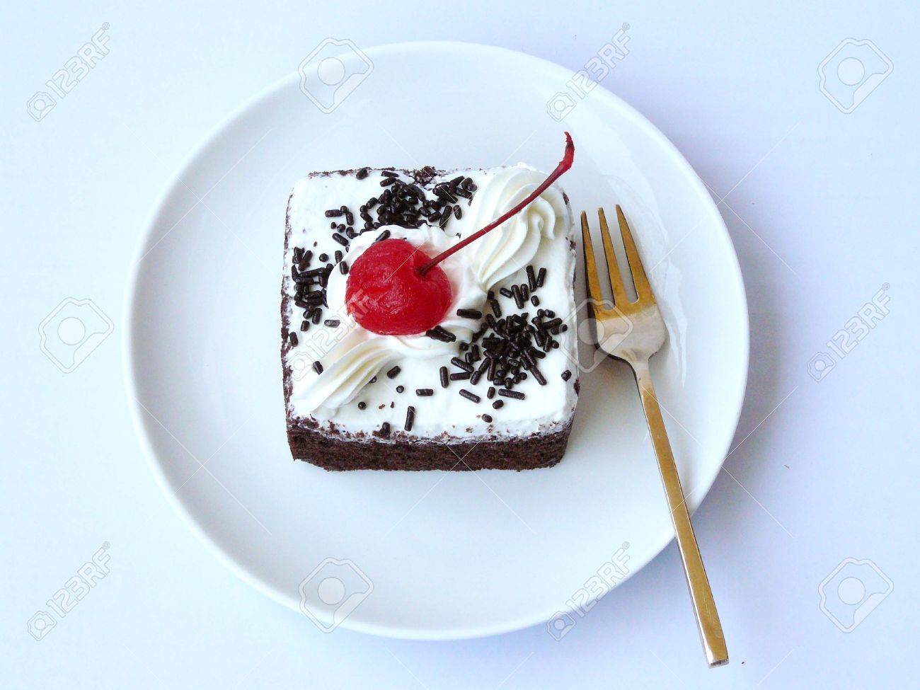 チョコレート ケーキ チョコレート おいしいのミニ シフォン シフォン ケーキがミルク クリームと赤で飾られた真鍮のフォークと白いプレートの桜 白い背景で隔離のトップ ビューを閉じます の写真素材 画像素材 Image