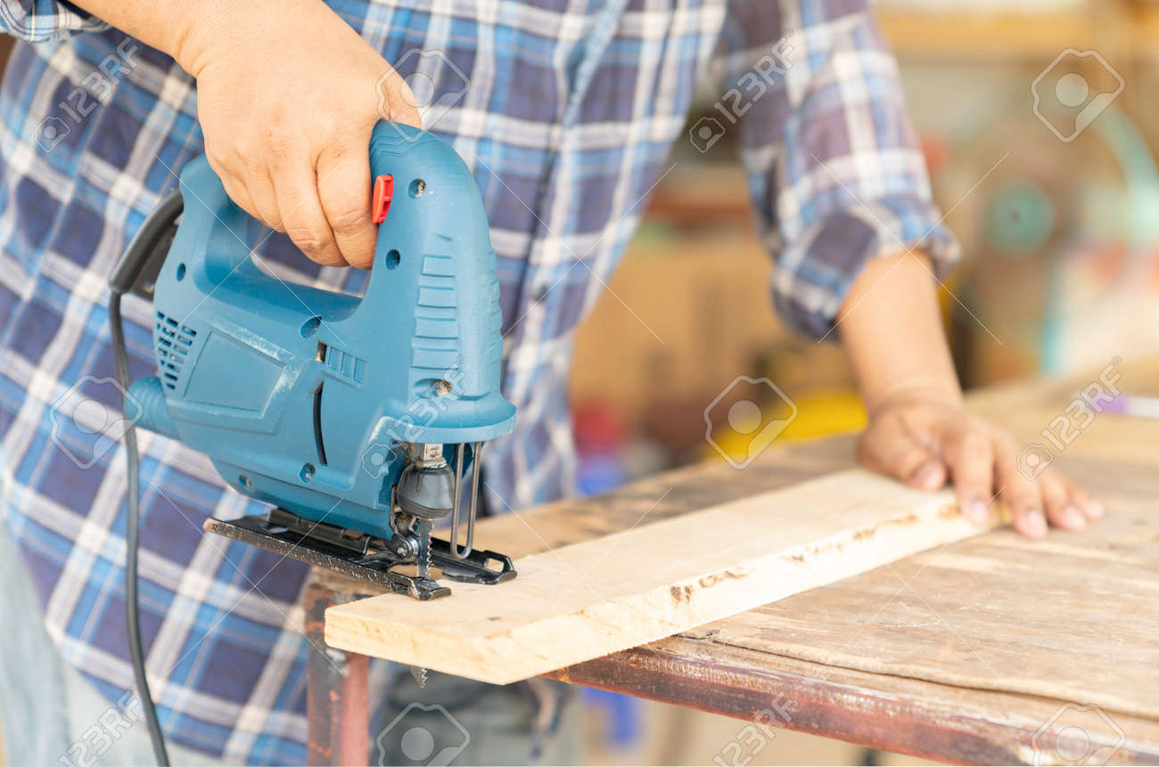 A Carpenter Uses An Electric Jigsaw To Cut Wooden Bars On The