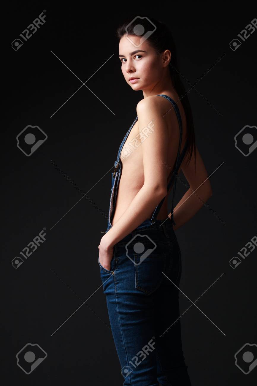 Mujer Morena Joven En Overoles Jeans Con El Torso Desnudo, De Pie, Mirando  A La Cámara, Vista Vuelta A Medias, Las Manos En Los Bolsillos, Fondo Gris  Fotos, retratos, imágenes y fotografía