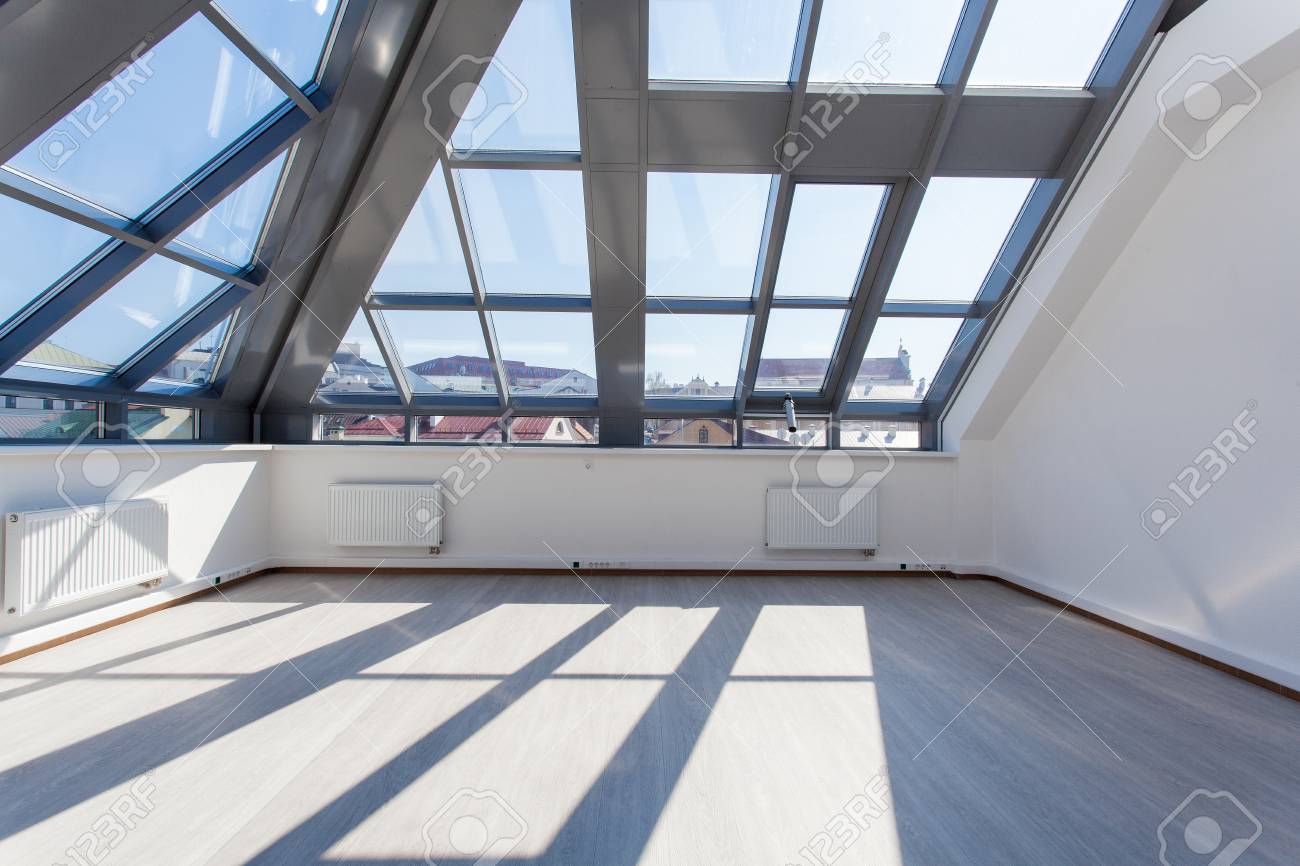 The Spacious Interior Room Unfurnished With A Glass Ceiling. Sunlight  Through Windows Cast Contrasting Shadows On The Floor. Urban Building And  Blue Sky In The Background. Фотография, картинки, изображения и  сток-фотография без
