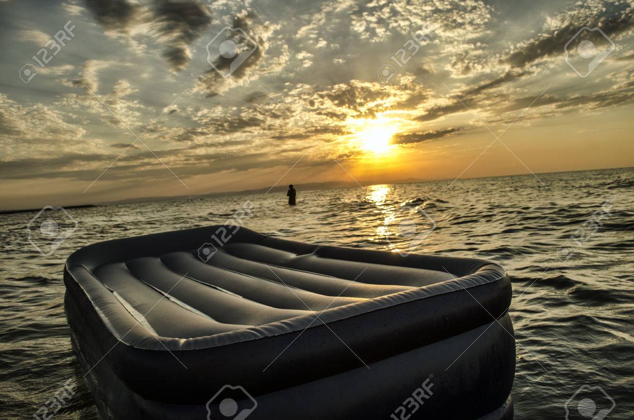 日没時にカスピ海の水で泳ぐ膨脹可能なマットレスの上で男のシルエット アプシェロン アゼルバイジャンのバクーで夏 の写真素材 画像素材 Image