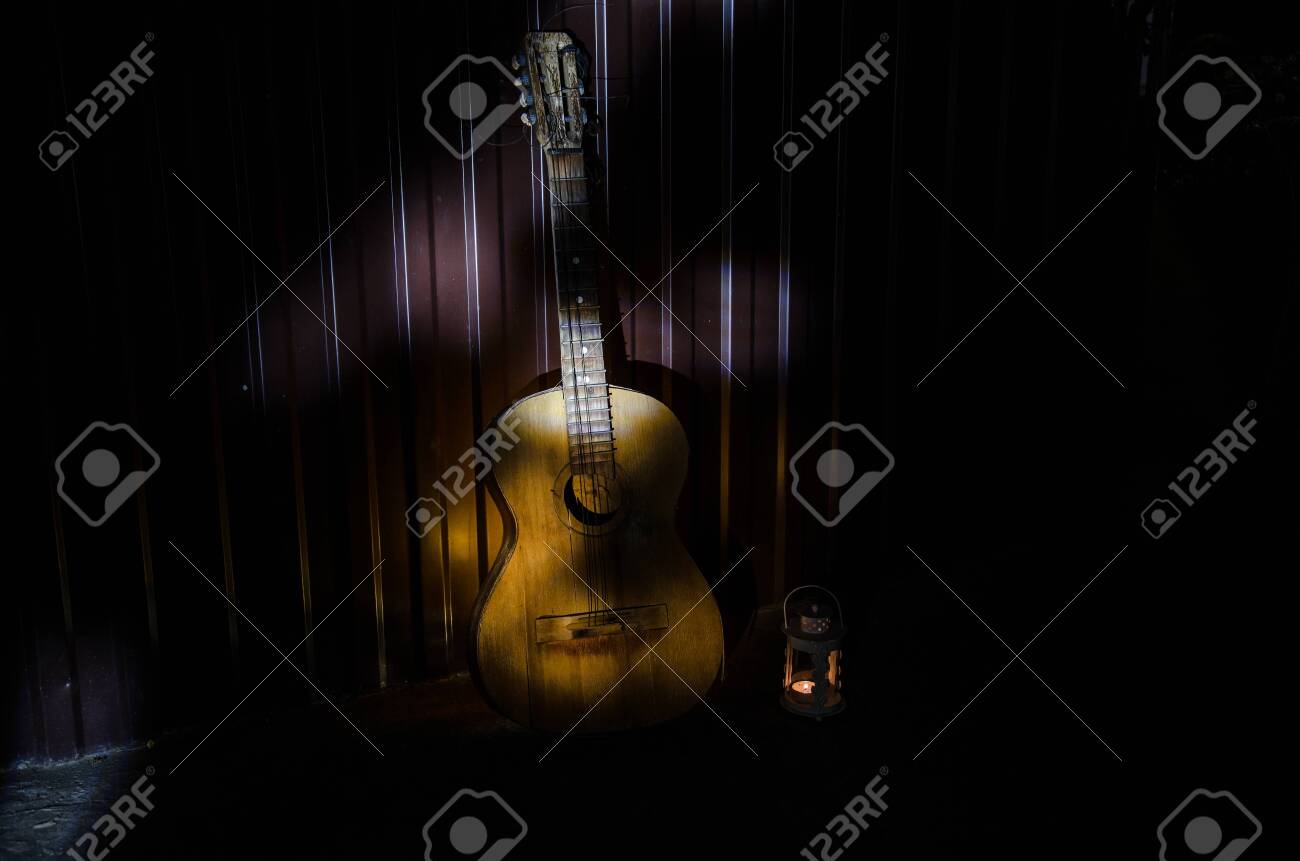 An wooden acoustic guitar is against a grunge textured wall. The room is dark with a spotlight for your copyspace. old broken guitar - 128832588 An wooden acoustic guitar is against a grunge textured wall. The room is dark with a spotlight for your copyspace. old broken guitar - 128832588