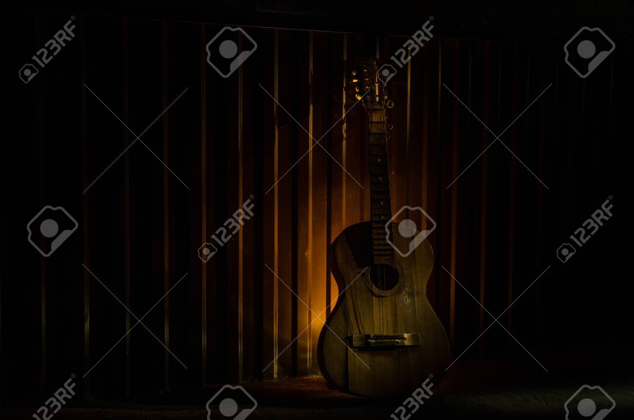 An wooden acoustic guitar is against a grunge textured wall. The room is dark with a spotlight for your copyspace. old broken guitar - 128832592 An wooden acoustic guitar is against a grunge textured wall. The room is dark with a spotlight for your copyspace. old broken guitar - 128832592