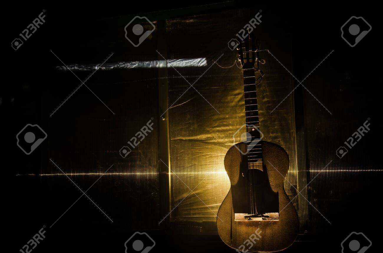 An wooden acoustic guitar is against a grunge textured wall. The room is dark with a spotlight for your copyspace. old broken guitar - 128917759 An wooden acoustic guitar is against a grunge textured wall. The room is dark with a spotlight for your copyspace. old broken guitar - 128917759