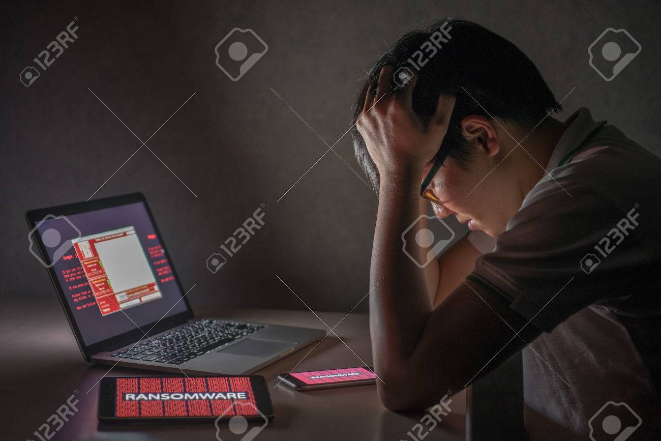 Young Asian male frustrated, confused and headache by WannaCry ransomware attack on desktop screen, notebook and smartphone, cyber attack internet security concept - 79239420 Young Asian male frustrated, confused and headache by WannaCry ransomware attack on desktop screen, notebook and smartphone, cyber attack internet security concept - 79239420