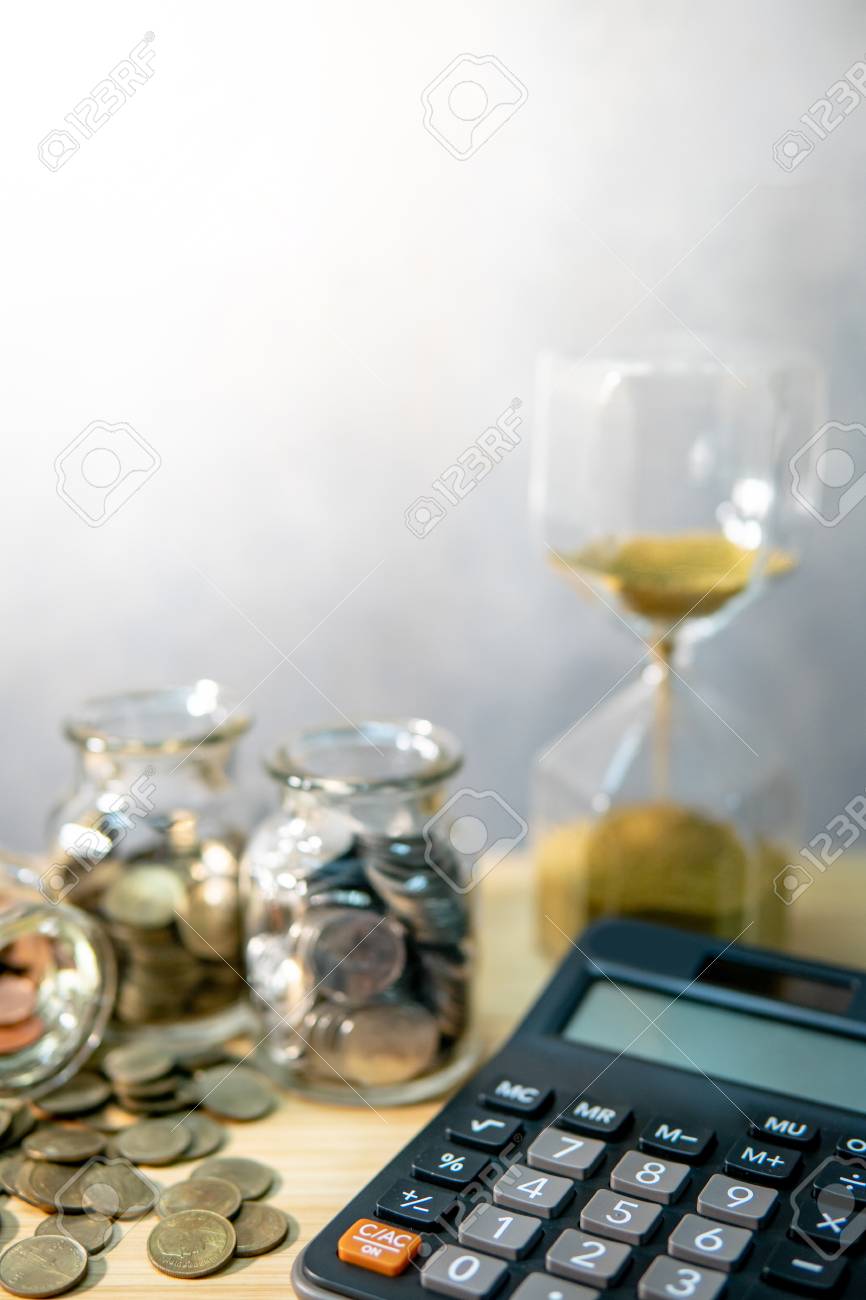 calculator with coin in currency glass jar and hourglass on wooden