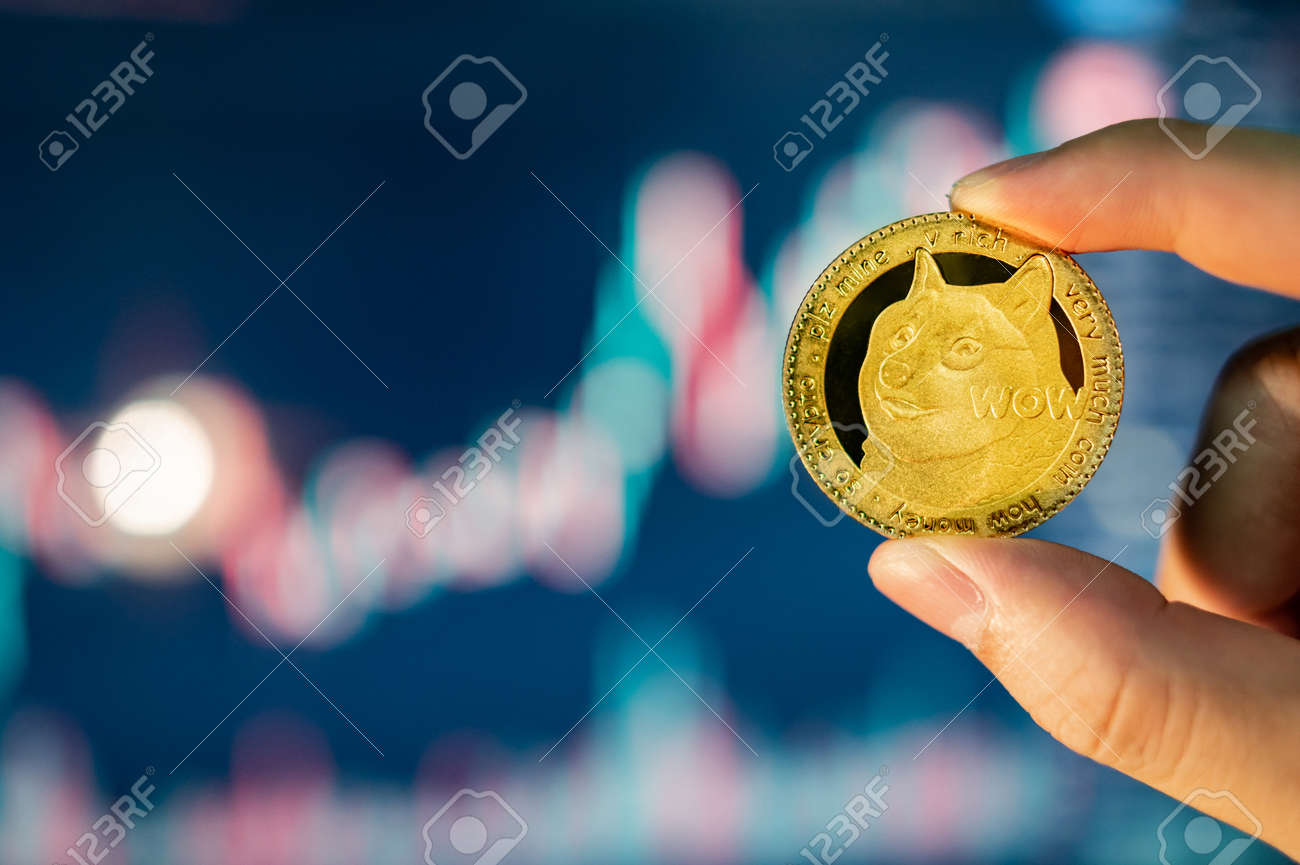 배경에 흐릿한 촛대 차트가 있는 금 도지코인을 손에 들고 있습니다. Doge는 암호화폐 세계에서 가장 인기 있는 밈 코인입니다. 로열티  무료 사진, 그림, 이미지 그리고 스톡포토그래피. Image 169738701