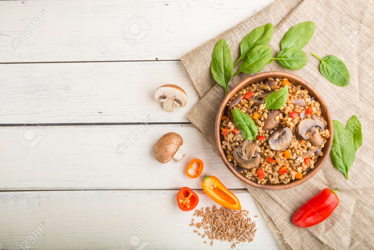 Spelt (dinkel wheat) porridge with vegetables and mushrooms in wooden bowl on a white wooden background and linen textile. Top view, flat lay, copy space. Russian traditional cuisine. - 157950294 Spelt (dinkel wheat) porridge with vegetables and mushrooms in wooden bowl on a white wooden background and linen textile. Top view, flat lay, copy space. Russian traditional cuisine. - 157950294