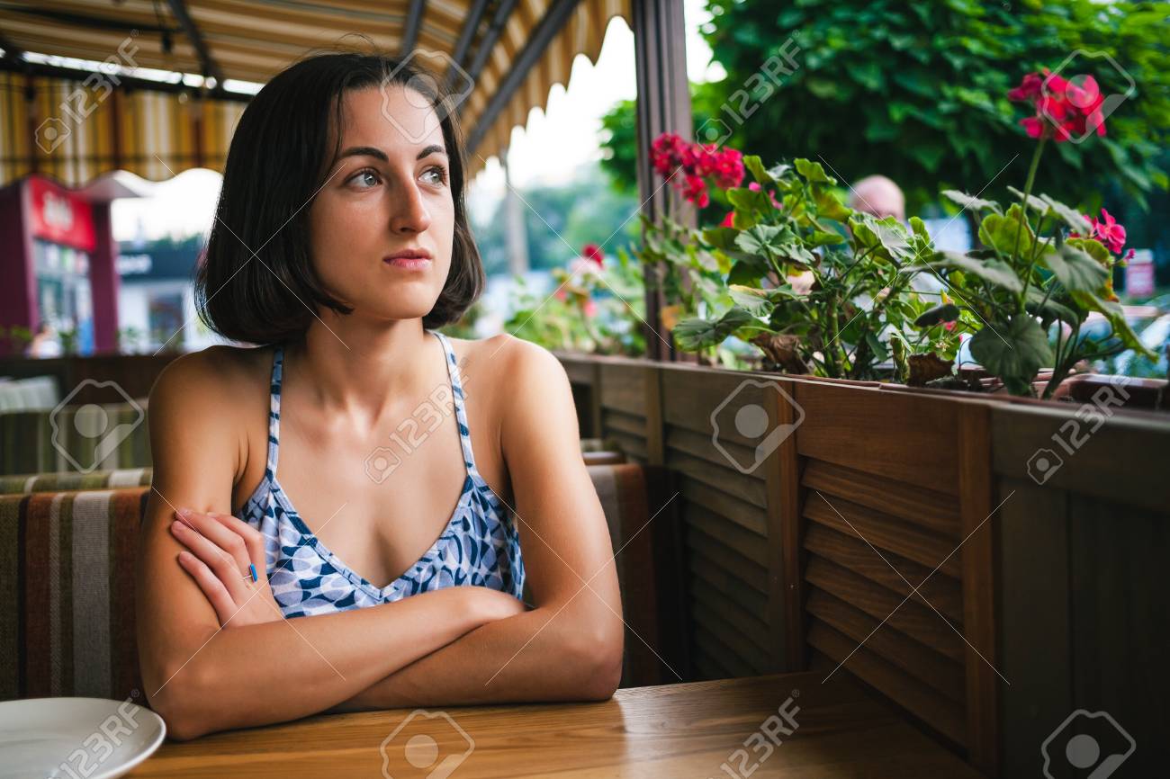 女の子がカフェで注文を待っている 女性がレストランのサマーテラスのテーブルに座っています ブルネットは彼女の注文を待っている周りに愚か者 の写真素材 画像素材 Image