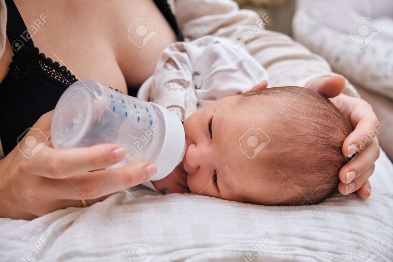 婦女哺乳 母親は、哺乳瓶からの混合物で生まれたばかりの赤ちゃんを養います。子供を養うための枕の上に男の子を持つ女性の写真素材・画像素材 Image  171751756