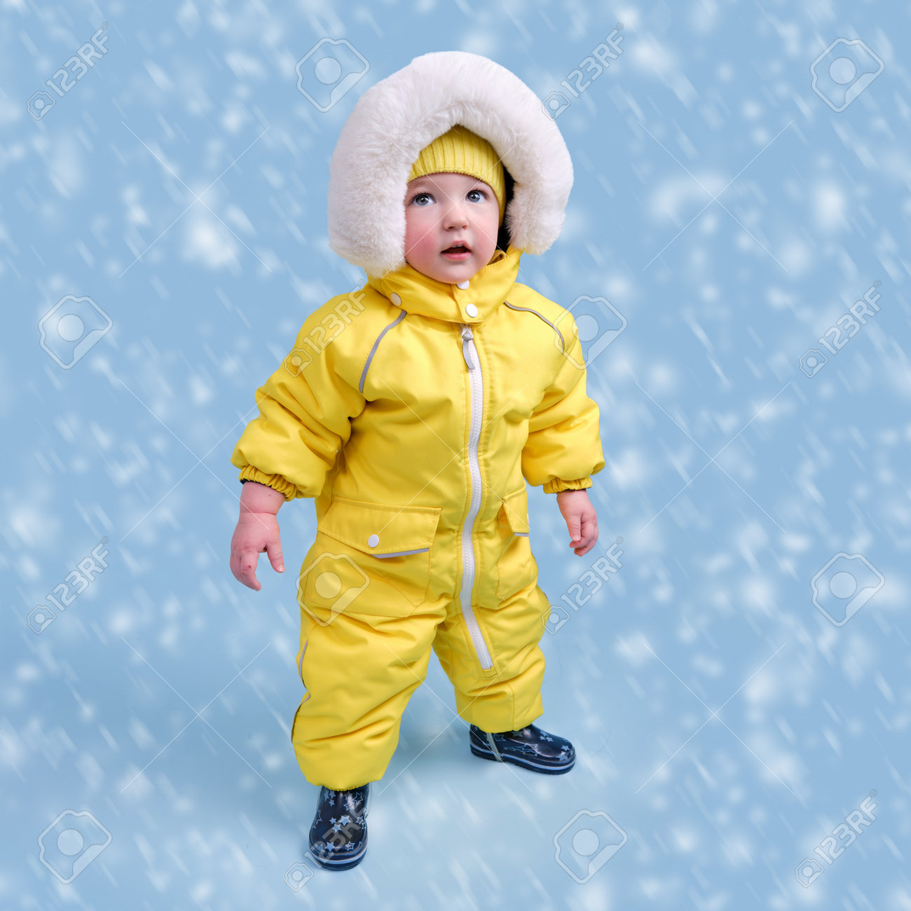 Happy Toddler Baby In Winter Clothes Snowsuit On Studio Blue