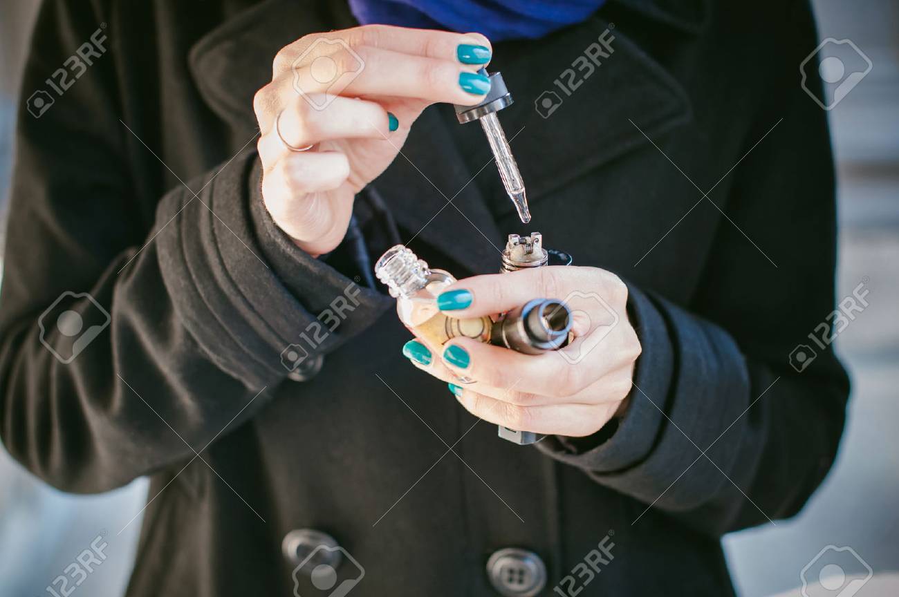 portrait of young beautiful woman with white hair, in a black coat, a skirt and a black hat, smoking an electronic cigarette, runs vape juice electronic cigarette. He holds a mechanical mod with RDA. - 70097542 portrait of young beautiful woman with white hair, in a black coat, a skirt and a black hat, smoking an electronic cigarette, runs vape juice electronic cigarette. He holds a mechanical mod with RDA. - 70097542