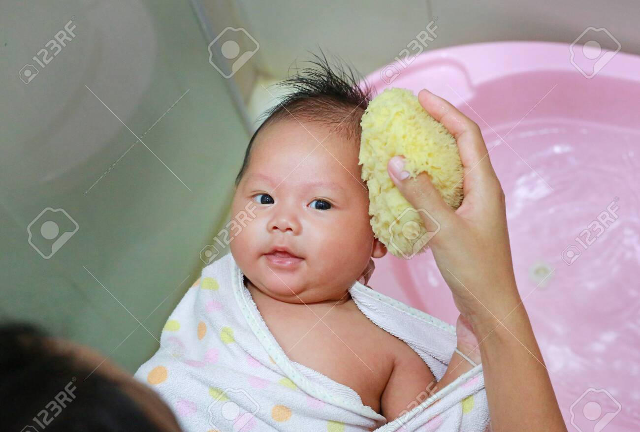 Close up hands of mother taking a bath to her newborn baby in a bathtub. - 128694574 Close up hands of mother taking a bath to her newborn baby in a bathtub. - 128694574
