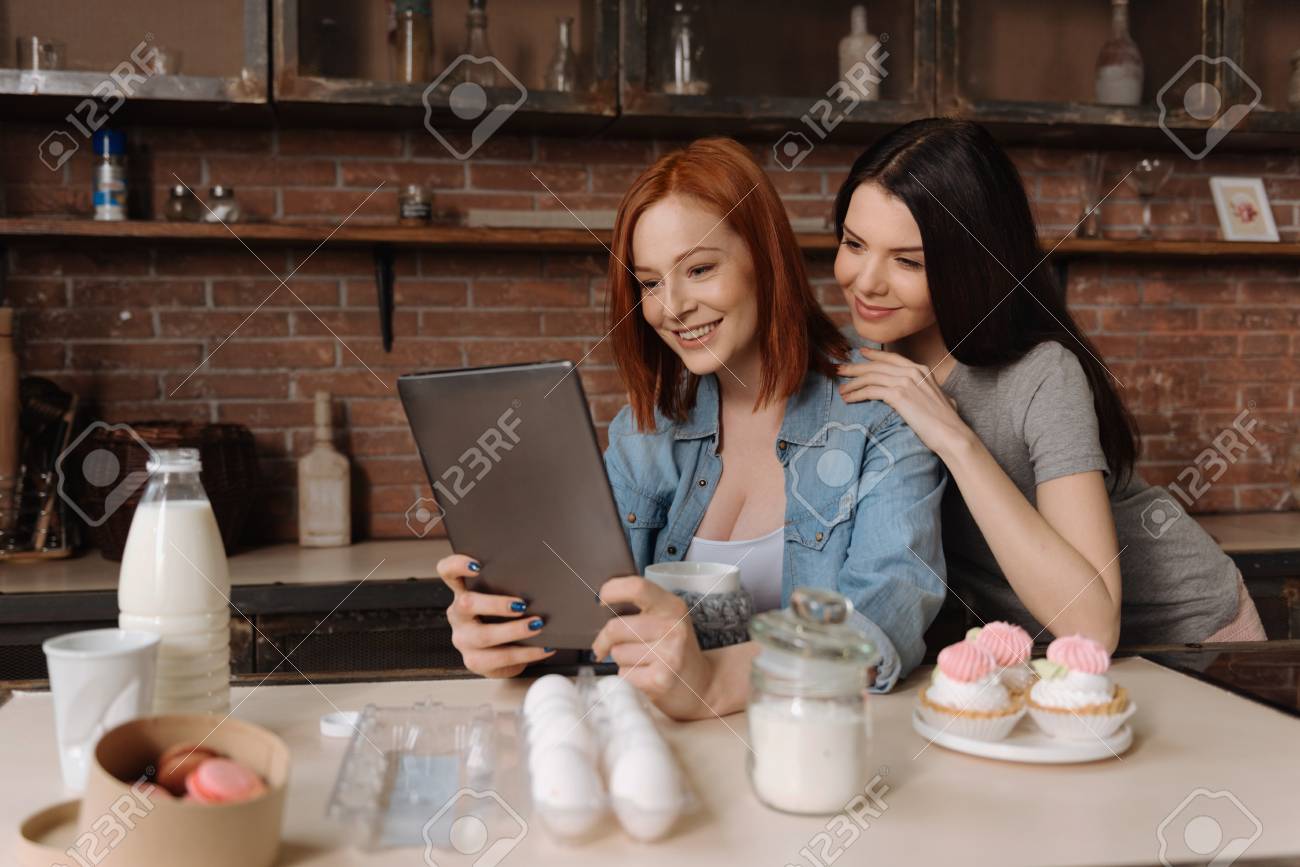 最高のバリアントです 横向きポーズのタブレットで見ながら彼女の友人の肩に手を置くとかわいい笑顔ブルネット の写真素材 画像素材 Image
