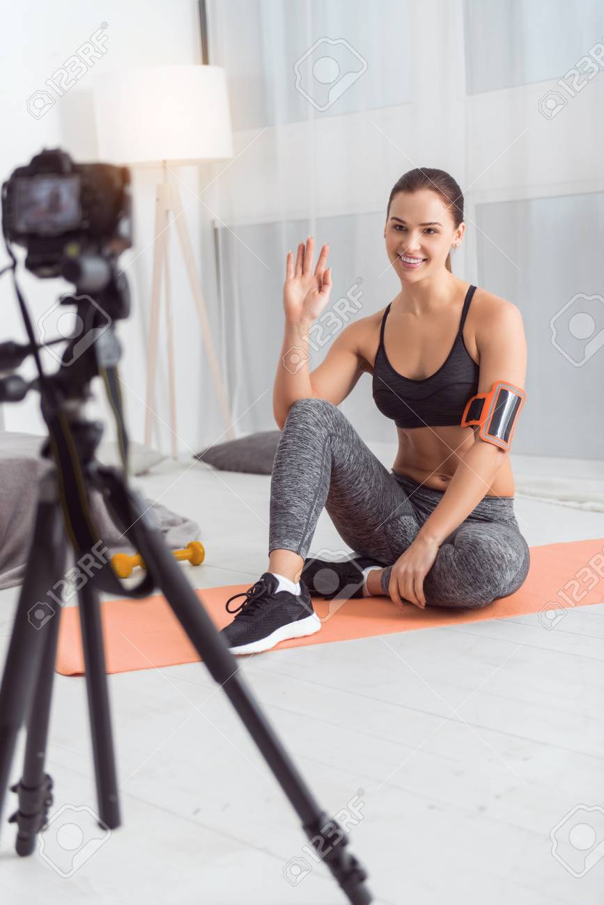 Hola Chicos. Atractiva Joven Blogger Atlética De Cabello Oscuro Sonriendo Y Vistiendo Ropa Deportiva Mientras Hace Un Video Fotos, Retratos, Imágenes Y Fotografía De Libres De Derecho. Image 94992415.
