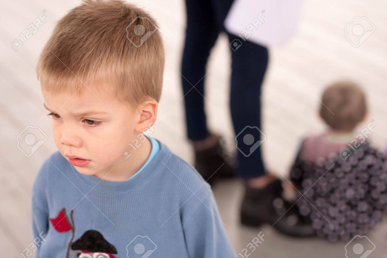 sad blond boy jealous about being neglected by his mother or caregiver who is giving attention to another child - 47052453 sad blond boy jealous about being neglected by his mother or caregiver who is giving attention to another child - 47052453