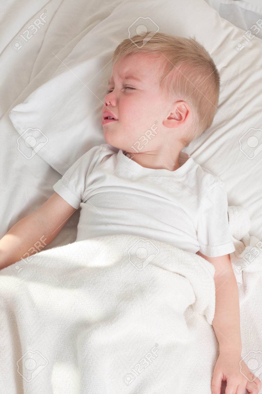 a sick blond toddler wearing white t-shirt lying in bed and crying - 47320499 a sick blond toddler wearing white t-shirt lying in bed and crying - 47320499