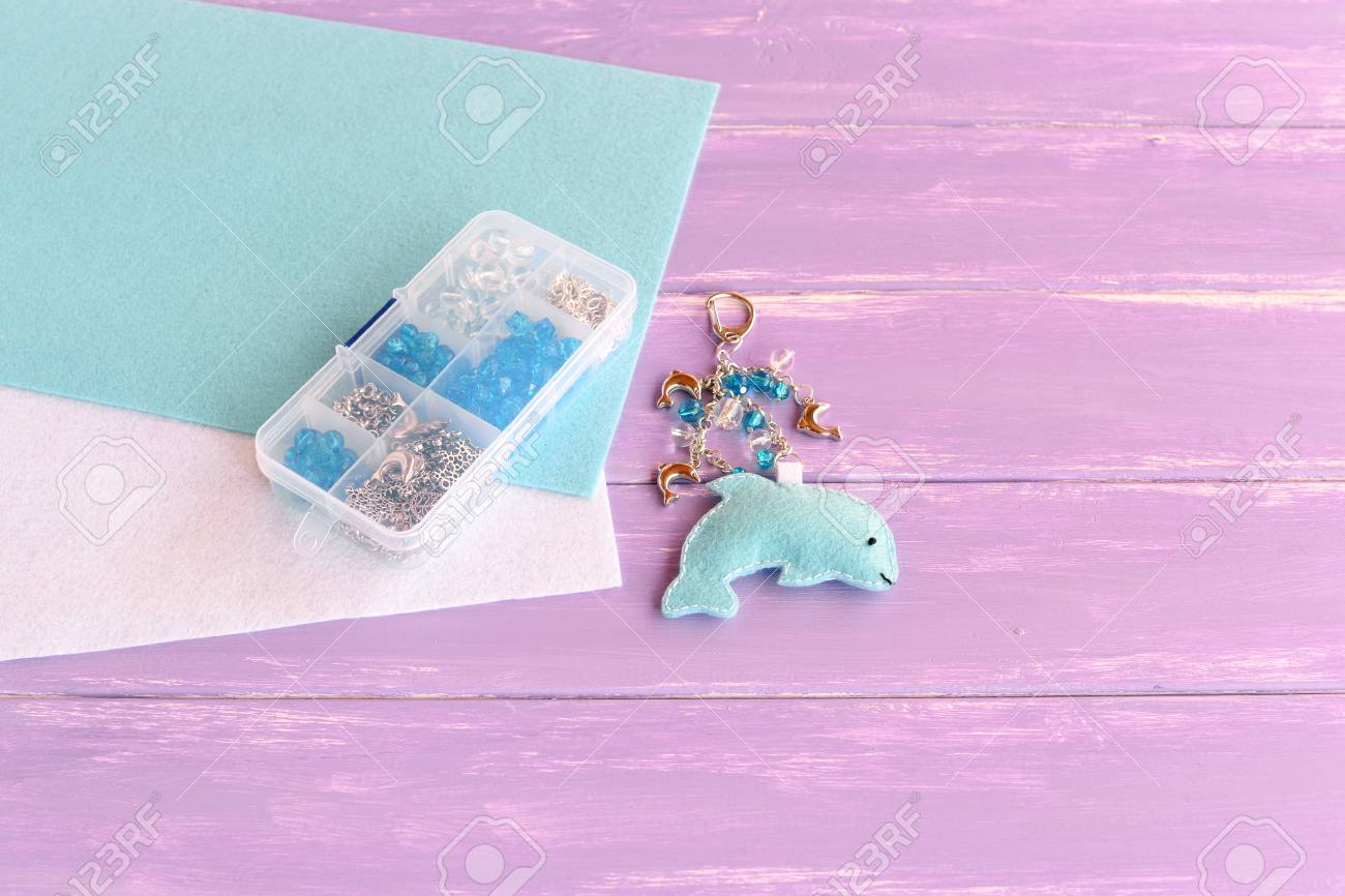 ビーズと面白いフェルト ドルフィン バッグ チャームの手作りフェルトのキーホルダー 簡単な子供の工芸品を縫製します 木製の背景 Diy 用品 の写真素材 画像素材 Image