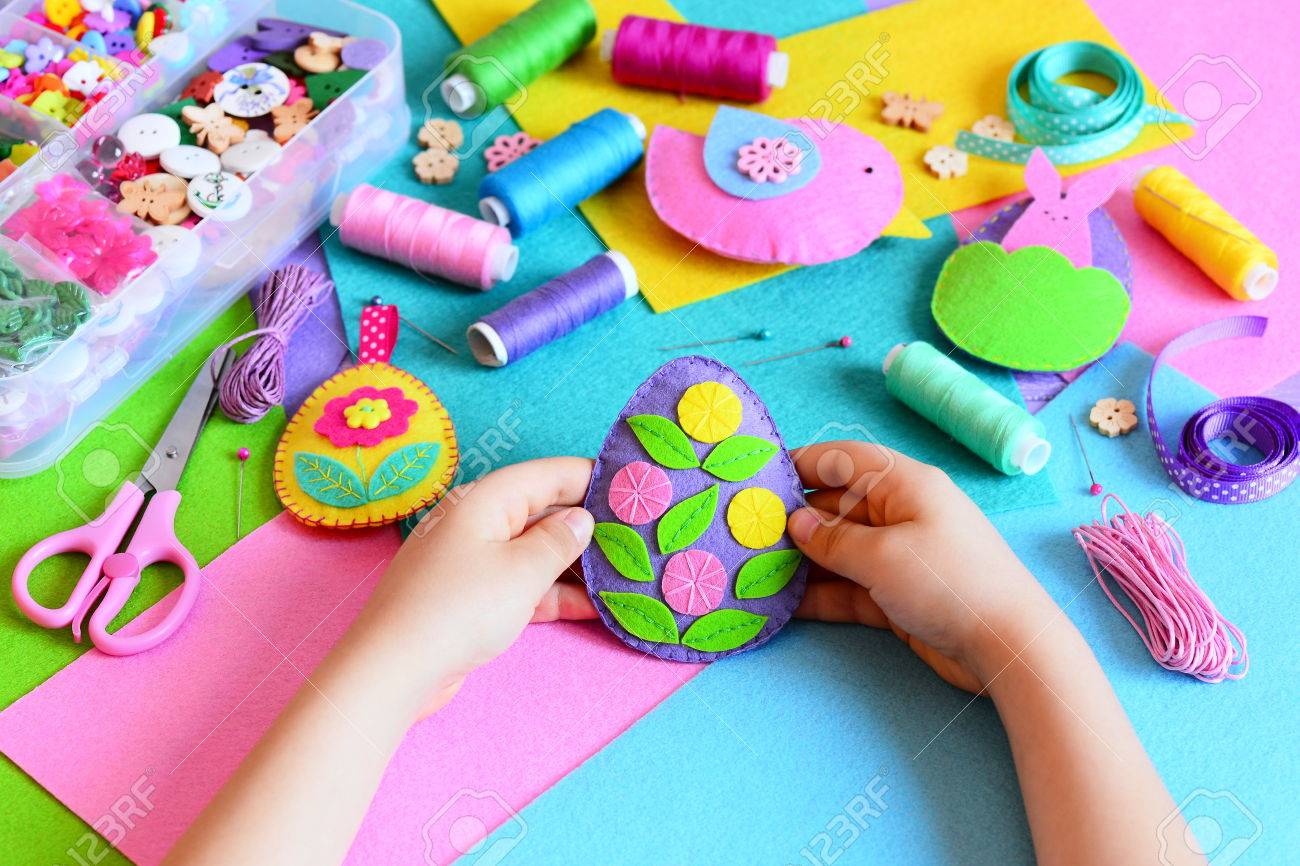 子は フェルトのイースターエッグの飾りをしました 小さな子供は 彼の手で感じたイースターエッグの飾りを保持します イースター クラフト クラフト ツールおよびテーブルの上材料 お祝い春工芸コンセプト の写真素材 画像素材 Image