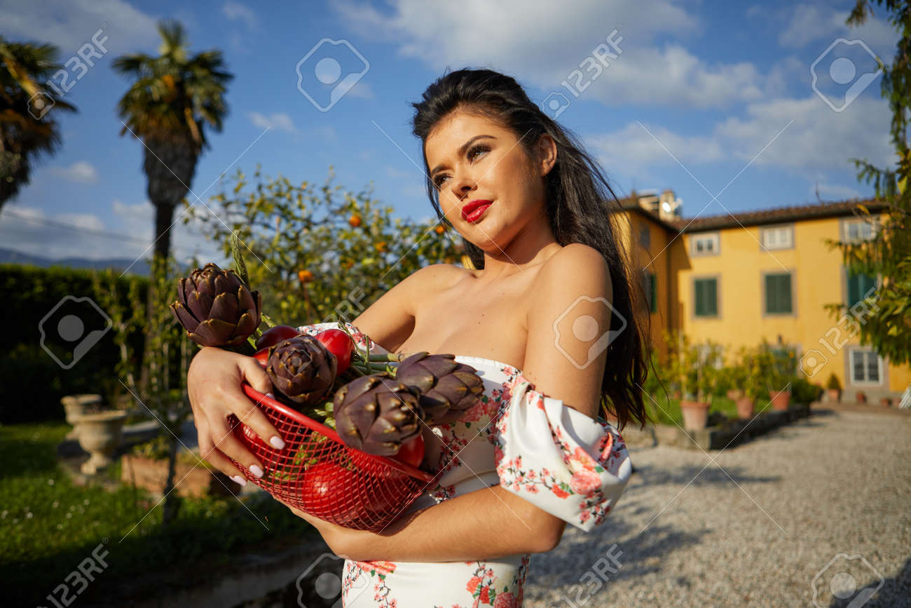 Woman holding basket of vegetables outdoors at her garden. italian life style - 166052447 Woman holding basket of vegetables outdoors at her garden. italian life style - 166052447