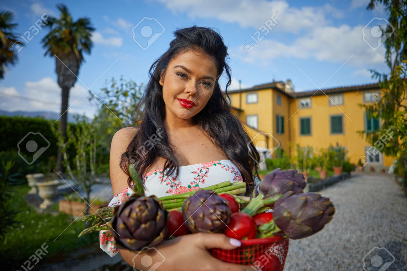 Woman holding basket of vegetables outdoors at her garden. italian life style - 166052450 Woman holding basket of vegetables outdoors at her garden. italian life style - 166052450